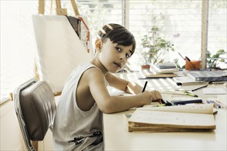 Boy sitting in his drawing class. looking seriously out of the corner of his eye at the camera. Creativity is shown through the act of drawing