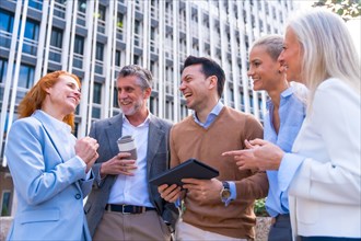 Cheerful group of coworkers laughing and looking at a tablet outdoors in a corporate office area