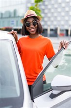 Summer vibes: young black woman in orange shirt and sunglasses getting into car with a smile