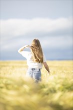 A young girl walks through a cornfield on a sunny warm day and strokes her hair