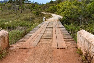 Dirt road with rustic and primitive wooden bridge between hills and the vegetation of the Biribiri environmental reserve in Diamantina