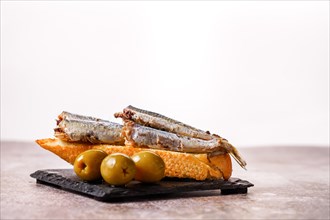 Tapa of sardines with tomato and olives on black slate and white background typical Spanish