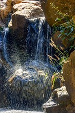 Small waterfall with waters running and shining between rocks and vegetation
