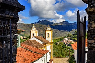 Beautiful historic church in the city of Ouro Preto seen between old stone portals with the mountains in the background.