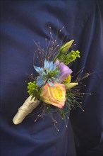Close up of flower clip called 'boutonniere' for groom attached to pocket of dark blue shirt made from beautiful natural roses and wild flowers