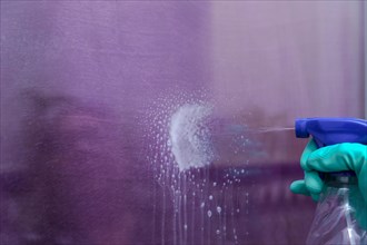 Close-up shot of a spray can of spray cleaner spraying liquid onto a glass pane