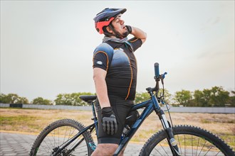 Male cyclist with neck pain outdoors. Sporty cyclist having neck pain while riding a bike