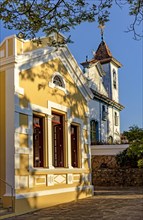 Historic baroque church next to a yellow neoclassical building lit by the afternoon sun in the city of Diamantina in Minas Gerais