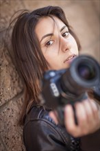 Young adult Iranian female photographer against wall holding camera