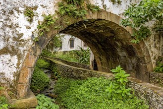 Old historical stone tunnel passing through vegetation and old colonial-style houses in the historic city of Ouro Preto in the state of Minas Gerais.