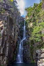 Stunning waterfall called Veu da Noiva between moss covered rocks and the vegetation of an area with nature preserved in the state of Minas Gerais