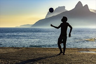 Boy playing soccer in front of the sea and hills during sunset