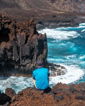 A young man sitting on the volcanic trail in the village of Tamaduste on the coast of the island of El Hierro