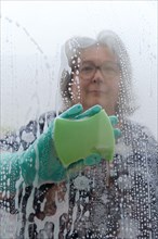 A woman cleans the glass with a green sponge and gloves