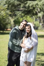 Pregnant woman in wedding dress posing with her partner outdoors