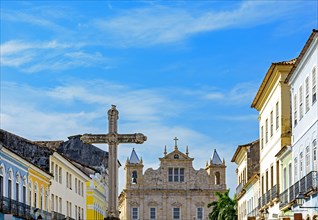 Large crucifix in the central square of the historic district of Pelourinho in the city of Salvador in Bahia with baroque church and colonial houses in the background