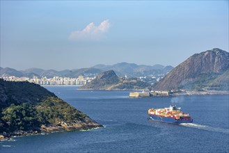 Cargo ship entering Guanabara Bay through the mountains and forests of Rio de Janeiro with the city of Niteroi in the background