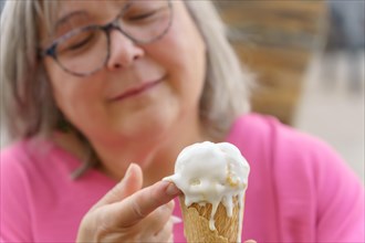 Close-up of a white-haired woman with glasses eating an ice cream with her fingers