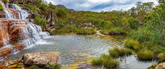 Panoramic view of waterfall and lake among the vegetation with mountains in background on Biribiri environmental reserve on Diamantina
