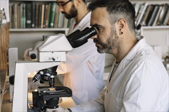 Scientist viewing sample through microscope during experiment in laboratory