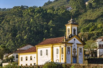 Facade of a historic baroque-style church in the city of Ouro Preto in Minas Gerais illuminated during the late afternoon with the hills and local vegetation