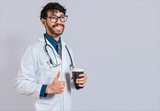 Young doctor holding a coffee to go isolated. Smiling doctor holding coffee with thumb up