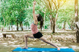 Young woman doing yoga warrior I pose. Girl practicing virabhadrasana yoga outdoors