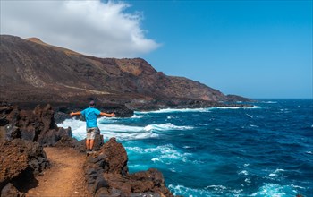 A young man walking on the volcanic path in the town of Tamaduste on the coast of the island of El Hierro