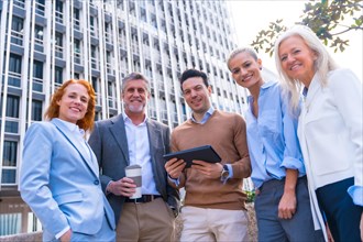 Portrait of cheerful group of coworkers laughing and looking at a tablet outdoors in a corporate office area