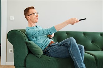 Man pointing tv remote control sitting on sofa in living room