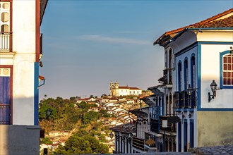 Streets and houses in the historic city of Ouro Preto in Minas Gerais with a church on top of the hill in the background.