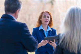 Collaborative and Innovative Red-Haired Female Business Professional Engaging in Teamwork with Colleagues through Digital Tablet while Participating in a Remote Business Meeting in a Modern Office Env...