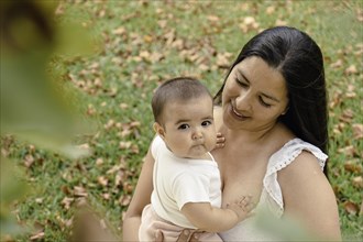 Portrait of attractive hispanic mother with her baby in a park. Baby looking at camera