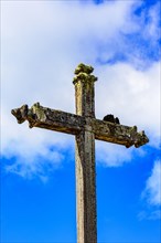 Ancient stone Catholic crucifix covered by parasitic plants and moss built in the late 17th century when the city of Lavras Novas in Minas Gerais appeared