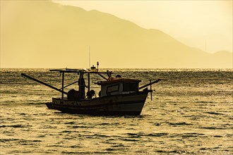 Wooden trawler used for fishing floating on the sea at sunset in Ilhabela on the coast of Sao Paulo