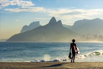 Boy with his bodyboard looking at the sea from Ipanema beach in Rio de Janeiro at dusk