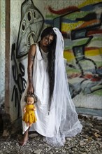 Deranged bride with a doll in abandoned place. Inspired by the traditional American legend of la llorona