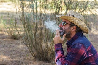 Man with beard and hat smoking a cigarette in the forest