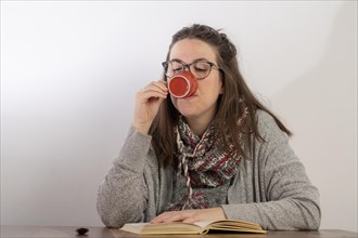 Young brunette woman with long hair and glasses drinking coffee while reading a book.white background and copy space