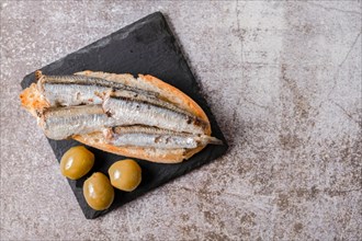 Tapa of sardines on a slice of bread with tomato and olives on black slate typical Spanish