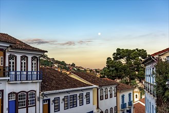 Old colonial style houses with their balconies in the traditional historic town of Ouro Preto during sunset with the moon in the background
