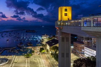Facade of the famous Lacerda elevator illuminated at night with city and boats in background in Salvador city