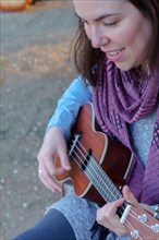 Top view of a young brunette girl with long hair playing the ukulele sitting in the grass