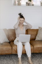 Woman sits on couch with laptop completely overwhelmed