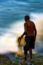 Motion blurred image with fisherman with his fishing net on rocks with mosses and the movement of sea waves