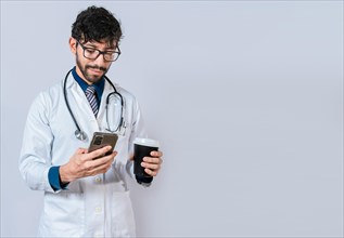 Young doctor holding a coffee to go and phone. Doctor with phone and holding coffee to go