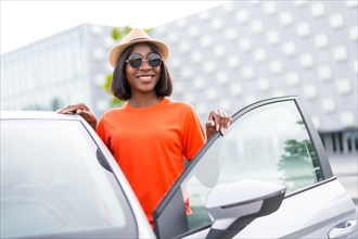Stylish summer: black woman in orange shirt and sunglasses opening car door with a smile