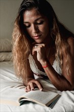 Latina woman concentrating and enjoying a book lying on her bed
