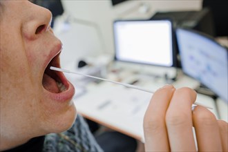 Symbol photo on the subject of ' Mandatory testing in the office'. A woman swabs her throat for a Sars Covid-19 antigen rapid test in front of her desk. Berlin