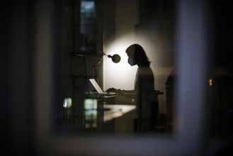 Symbolic photo on the subject of masks at the workplace. A woman sits in her desk in the office in the evening wearing an FFP2 mask. Berlin